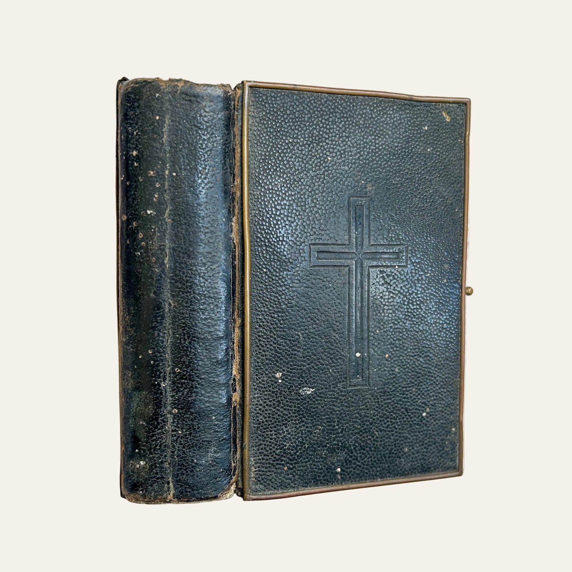 Vintage leather-bound book with a cross embossed on the cover, lying on a textured surface.