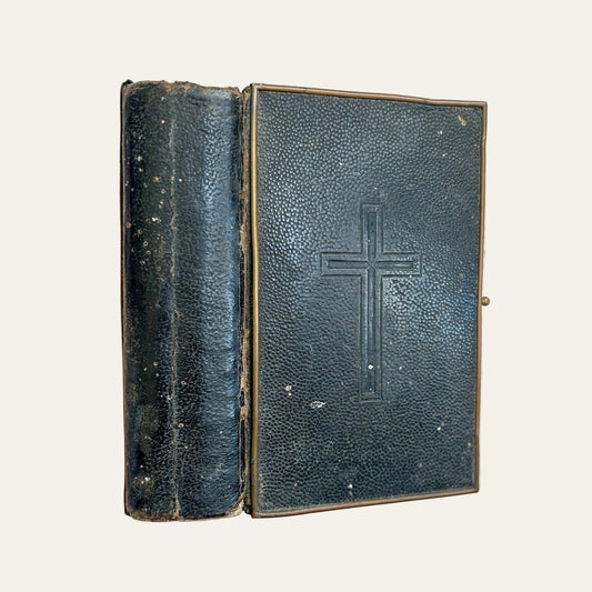 Vintage leather-bound book with a cross embossed on the cover, lying on a textured surface.