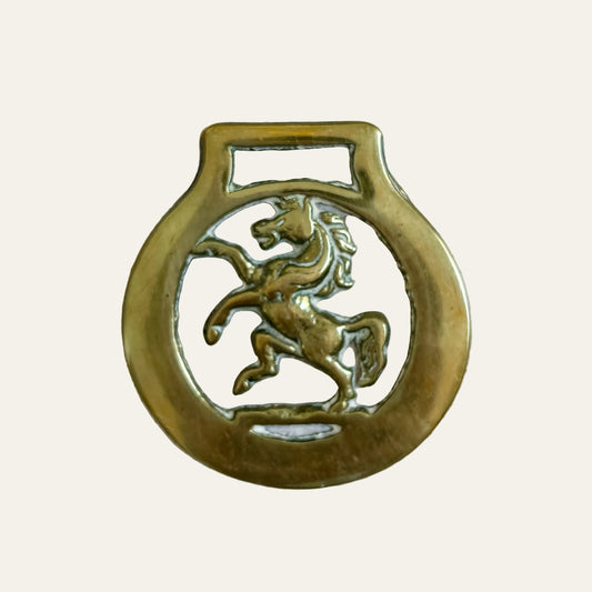 Brass badge with a horse emblem on a textured beige background