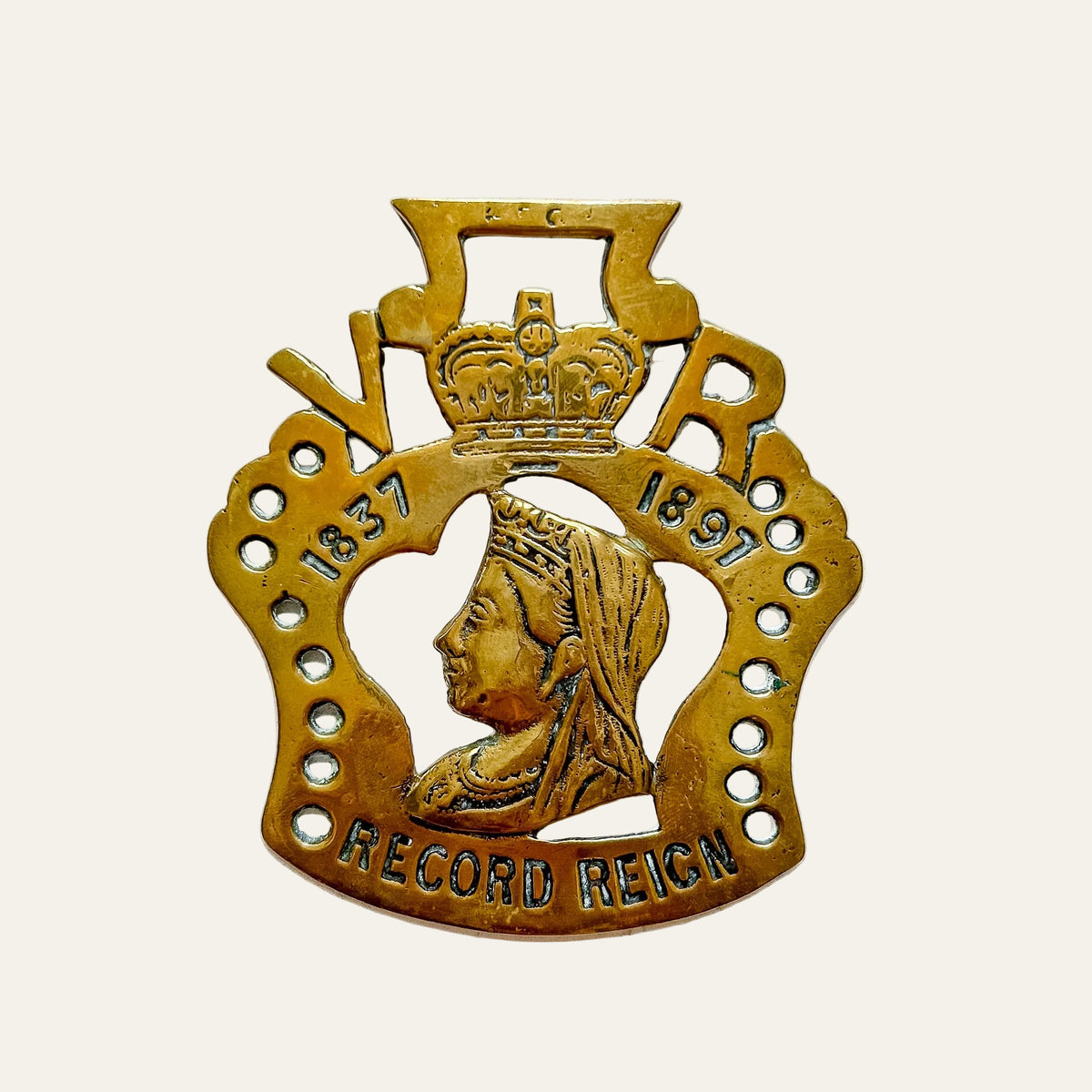 A brass commemorative badge featuring a profile portrait of Queen Victoria, a crown, and the text '1837', '1897', and 'RECORD REIGN' on a textured white background.
