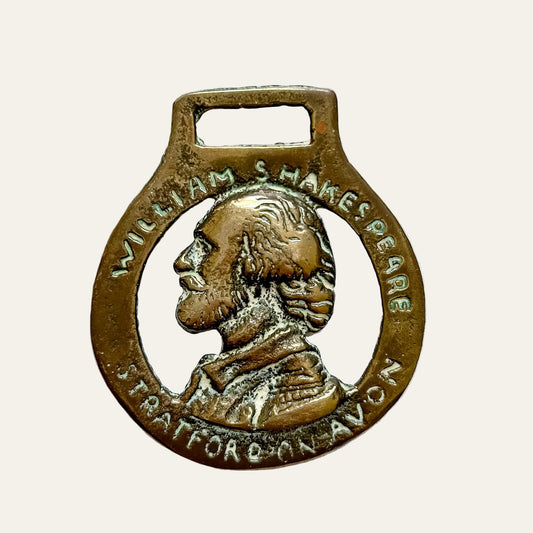 A vintage brass keyring or pendant featuring a profile portrait of William Shakespeare, with the text 'WILLIAM SHAKESPEARE' and 'STRATFORD ON AVON' engraved around the border, set against a textured white background.