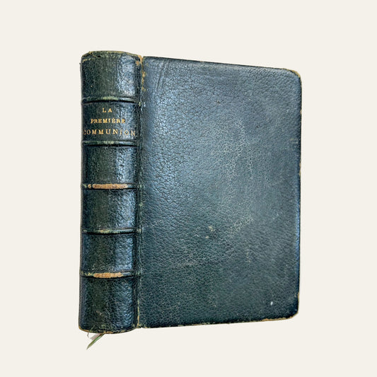 Vintage black leather book titled 'La Premiere Communion' on a textured beige surface