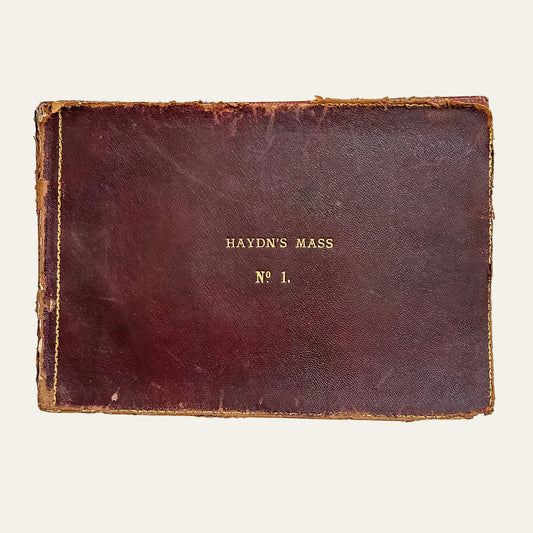 Vintage leather-bound book titled 'Haydn's Mass No. 1' on a textured white background