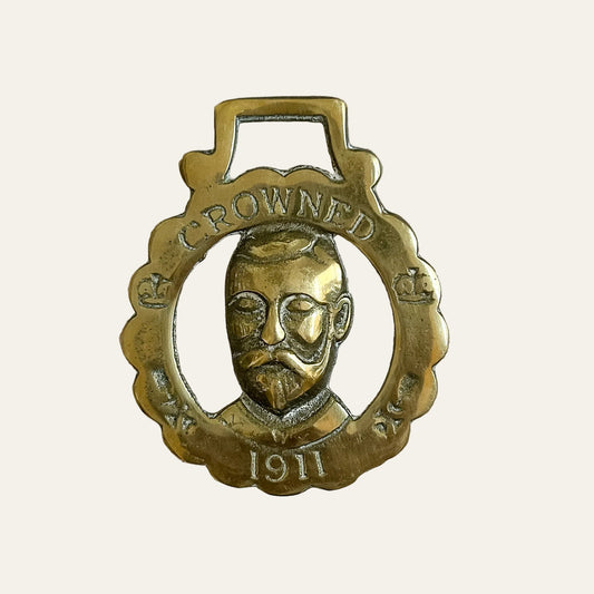Brass medallion with a face and 'Crowned' text on a textured beige background