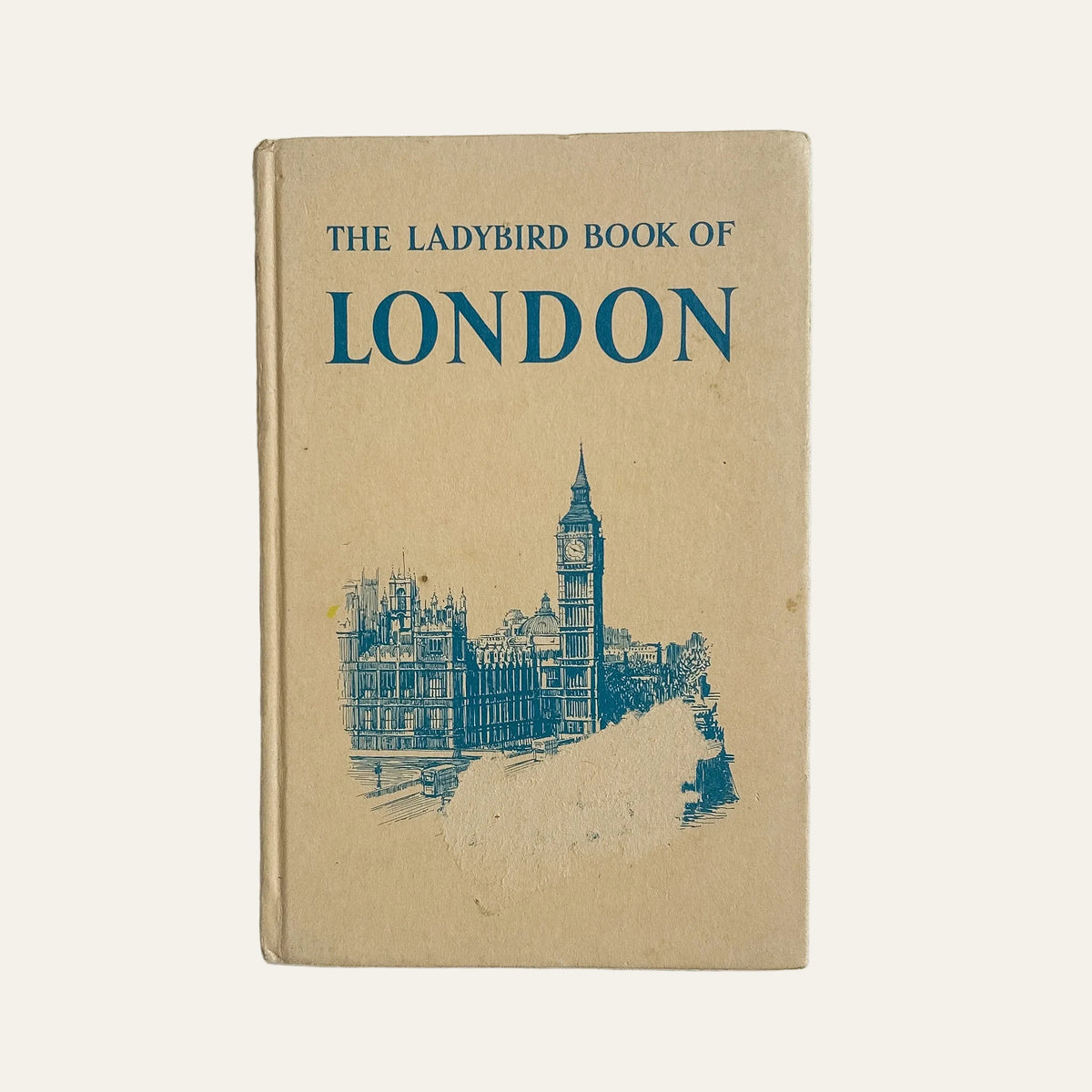 Vintage hardcover book titled 'The Ladybird Book of London' with a tan cover and blue text and illustration, photographed standing upright against a light textured wall.