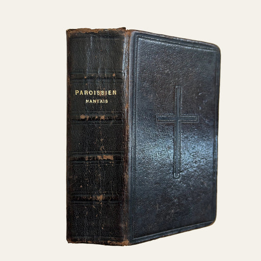 Vintage leather-bound book with a cross embossed on the cover, on a textured surface.